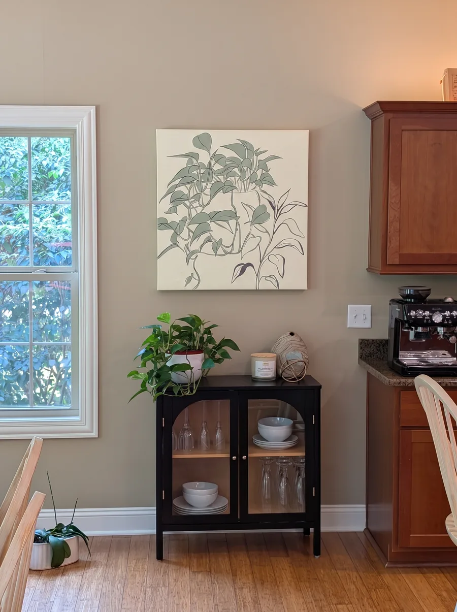 A cheerful kitchen nook with a botanical line-art canvas above a black display cabinet